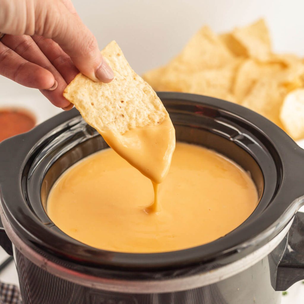 Nacho Cheese Dip in the slow cooker with a chip being dipped in