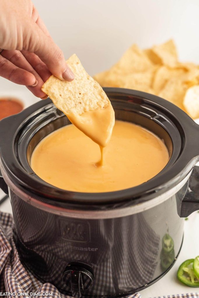 Nacho Cheese Dip in the slow cooker with a chip being dipped in