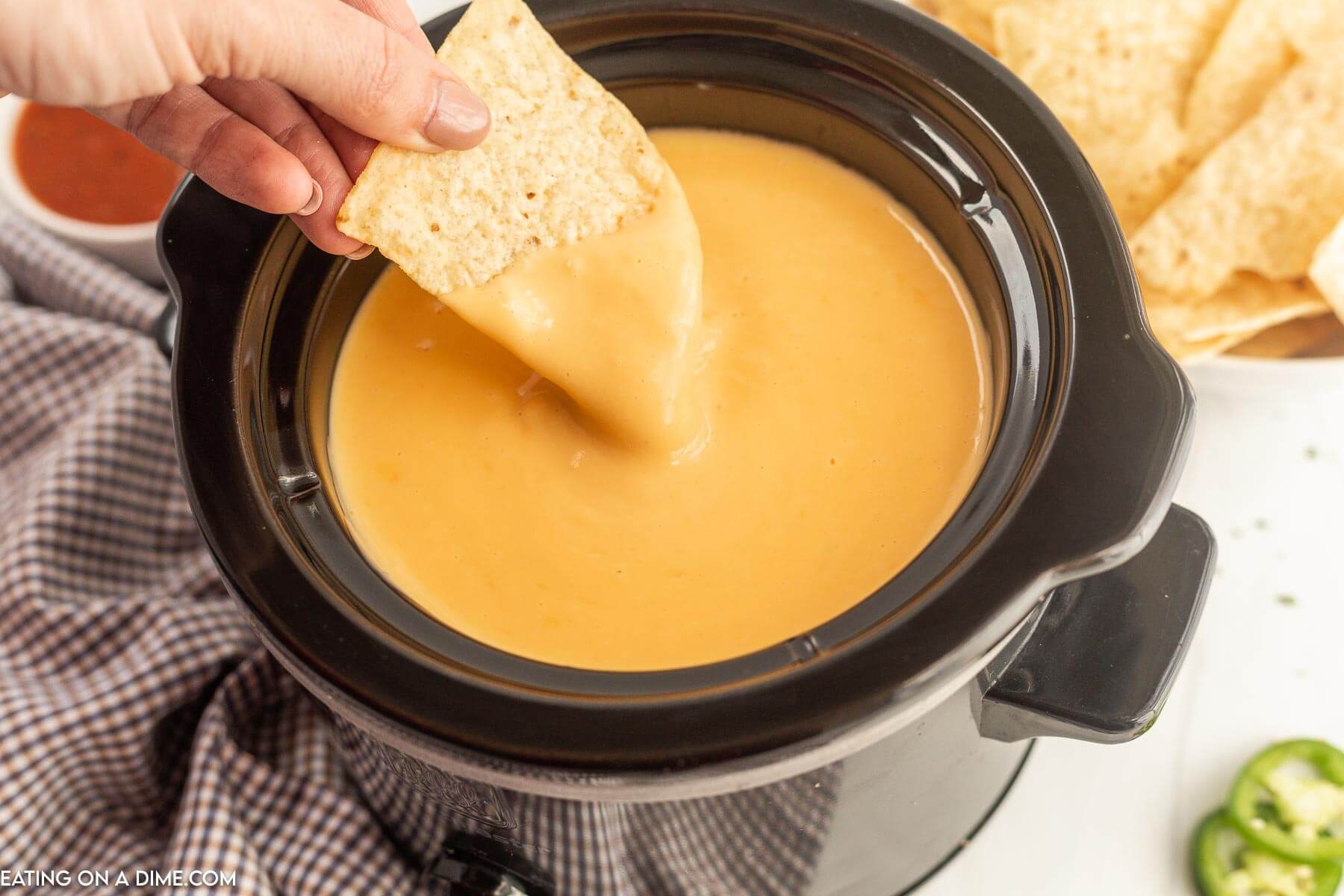 Nacho Cheese Dip in the slow cooker with a chip being dipped in