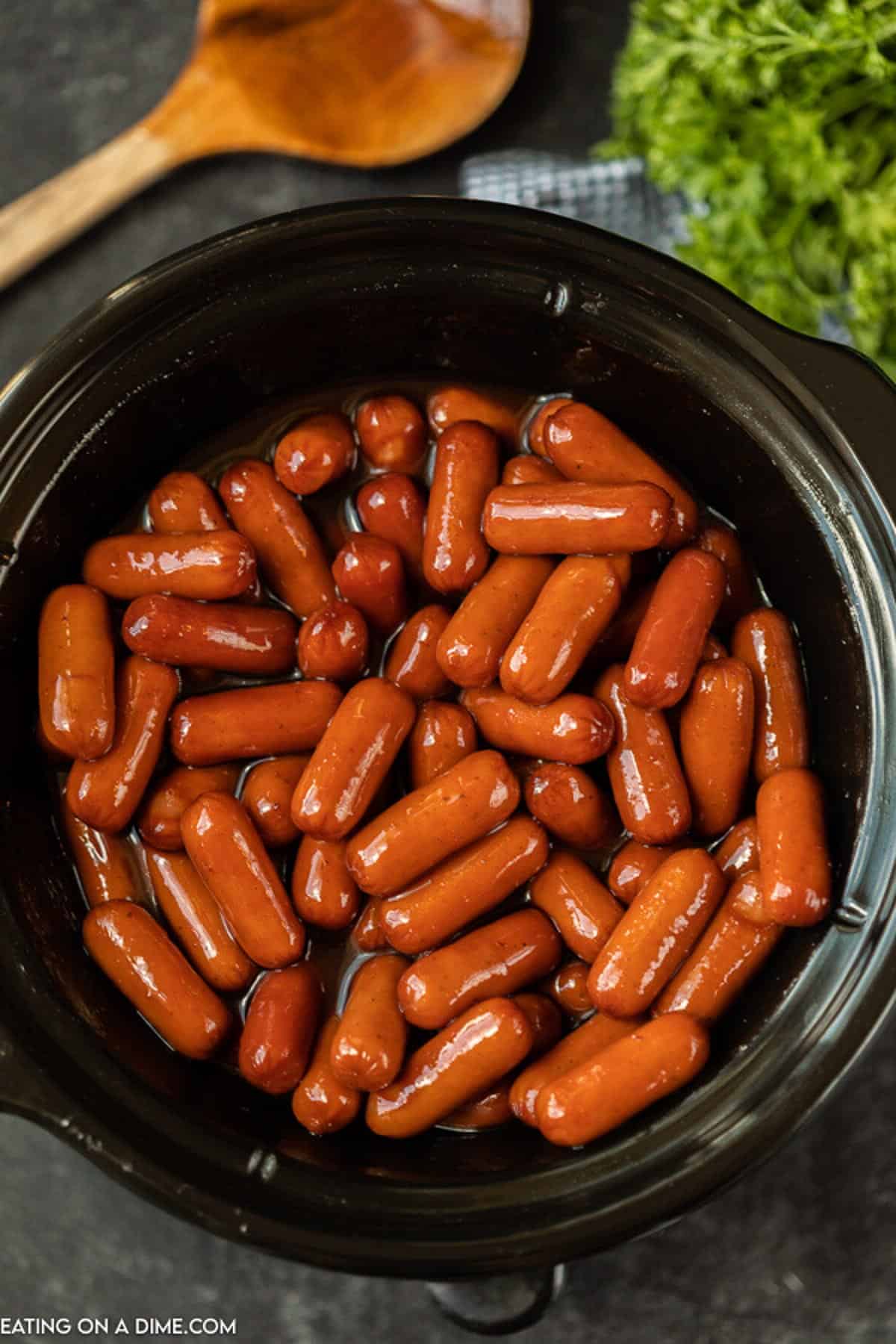 BBQ Little Smokies in a crock pot with a wooden spoon in it. 