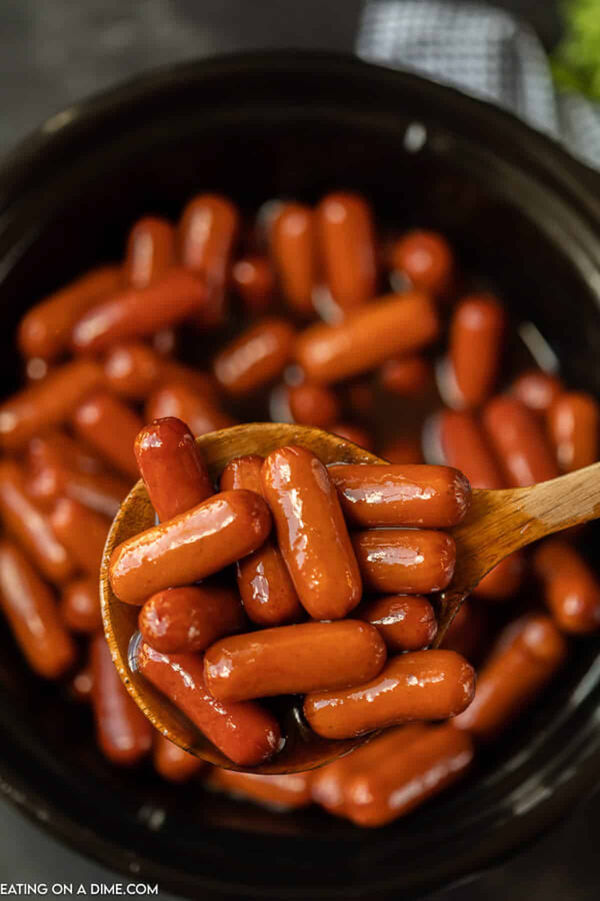 A large spoonful of BBQ little smokies being served out of a small crock pot. 
