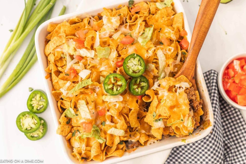 Walking Taco Casserole topped with slice jalapenos with a wooden spoon