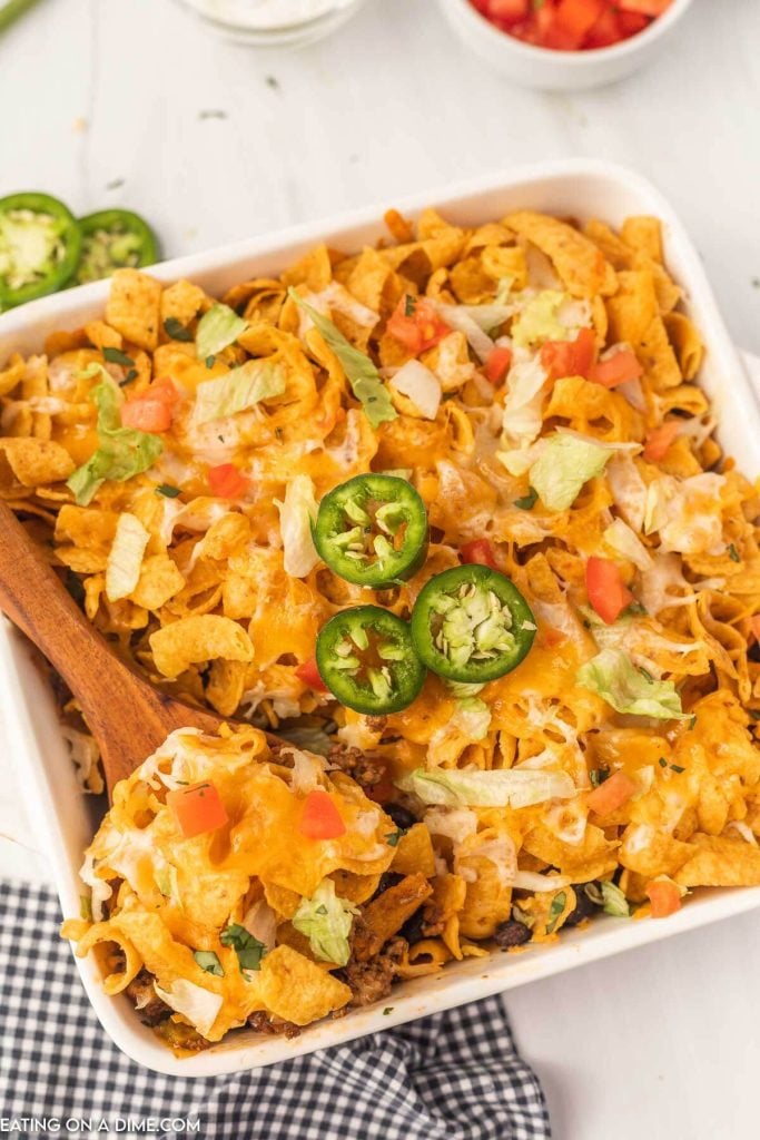 Walking Taco Casserole topped with slice jalapenos with a wooden spoon