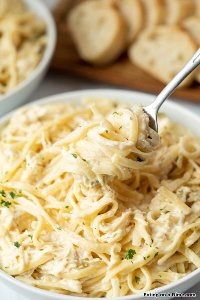 Close up image of a bowl of chicken alfredo with a bite on a fork
