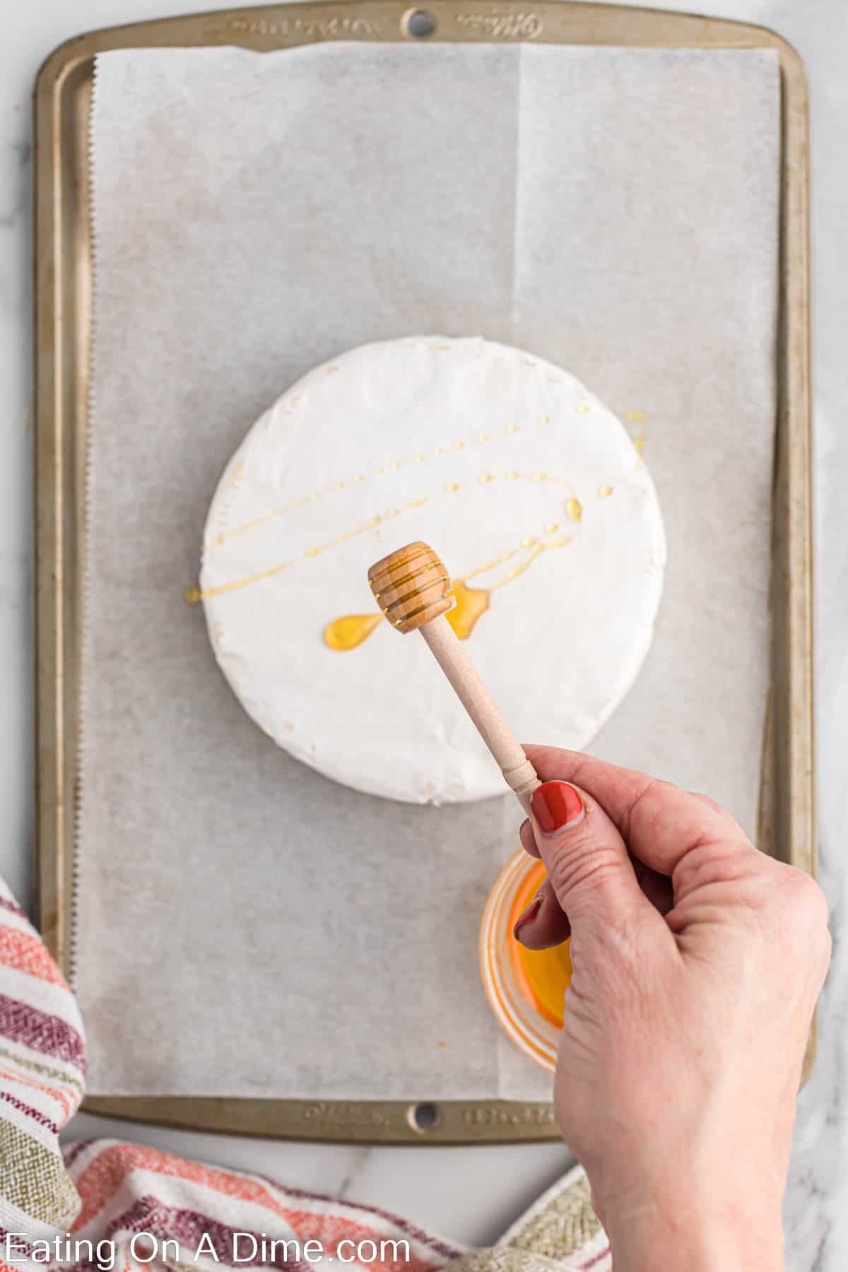 Honey being drizzled over brie on a baking sheet