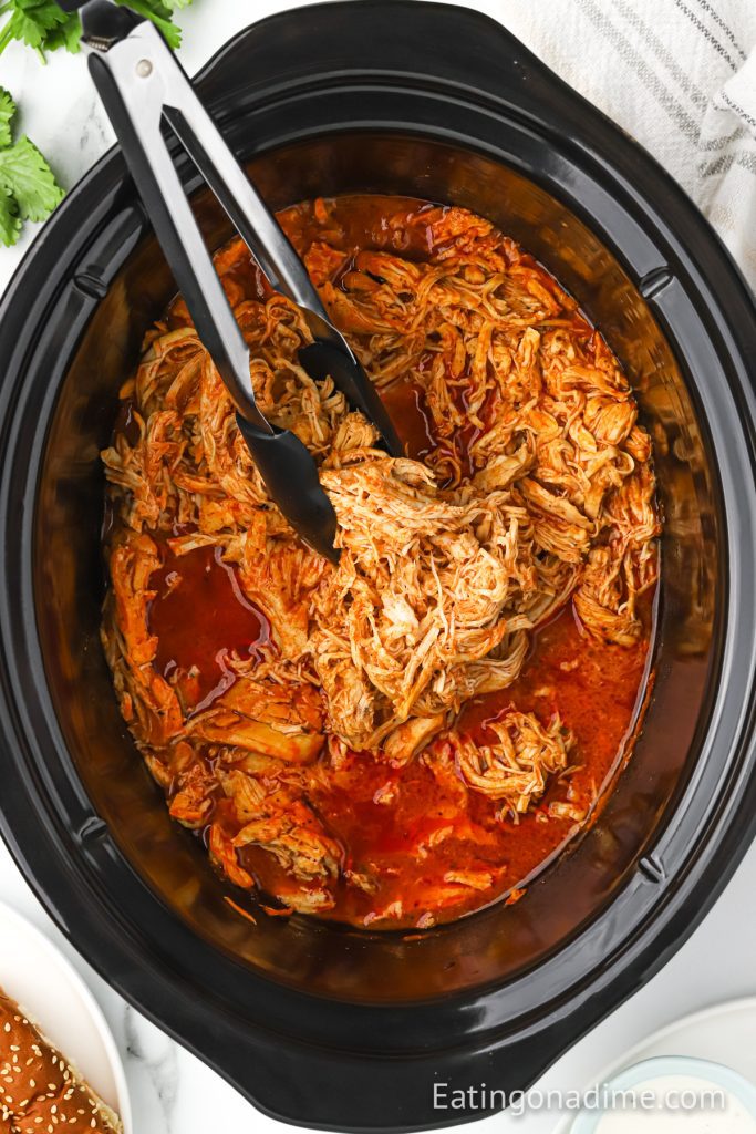 Buffalo Chicken in a slow cooker with some tongs