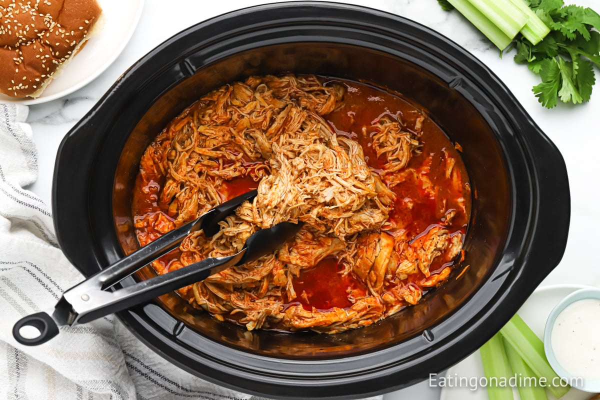 Buffalo Chicken in a slow cooker with some tongs