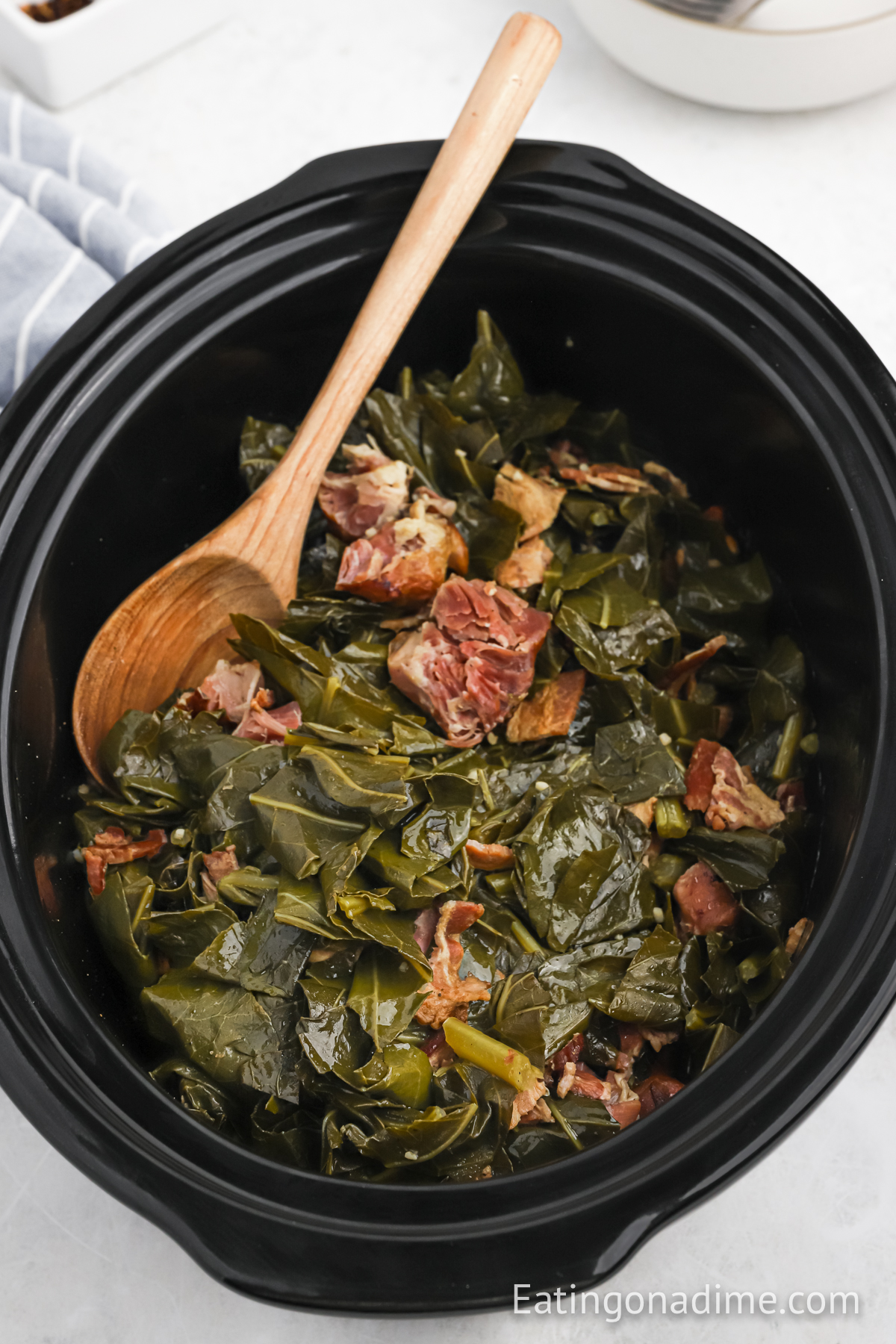 Collard greens with ham hock in the slow cooker with a wooden spoon