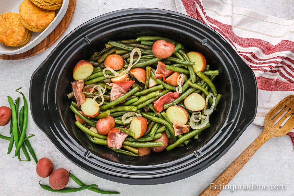 Green and potatoes in a crock pot with a wooden spoon