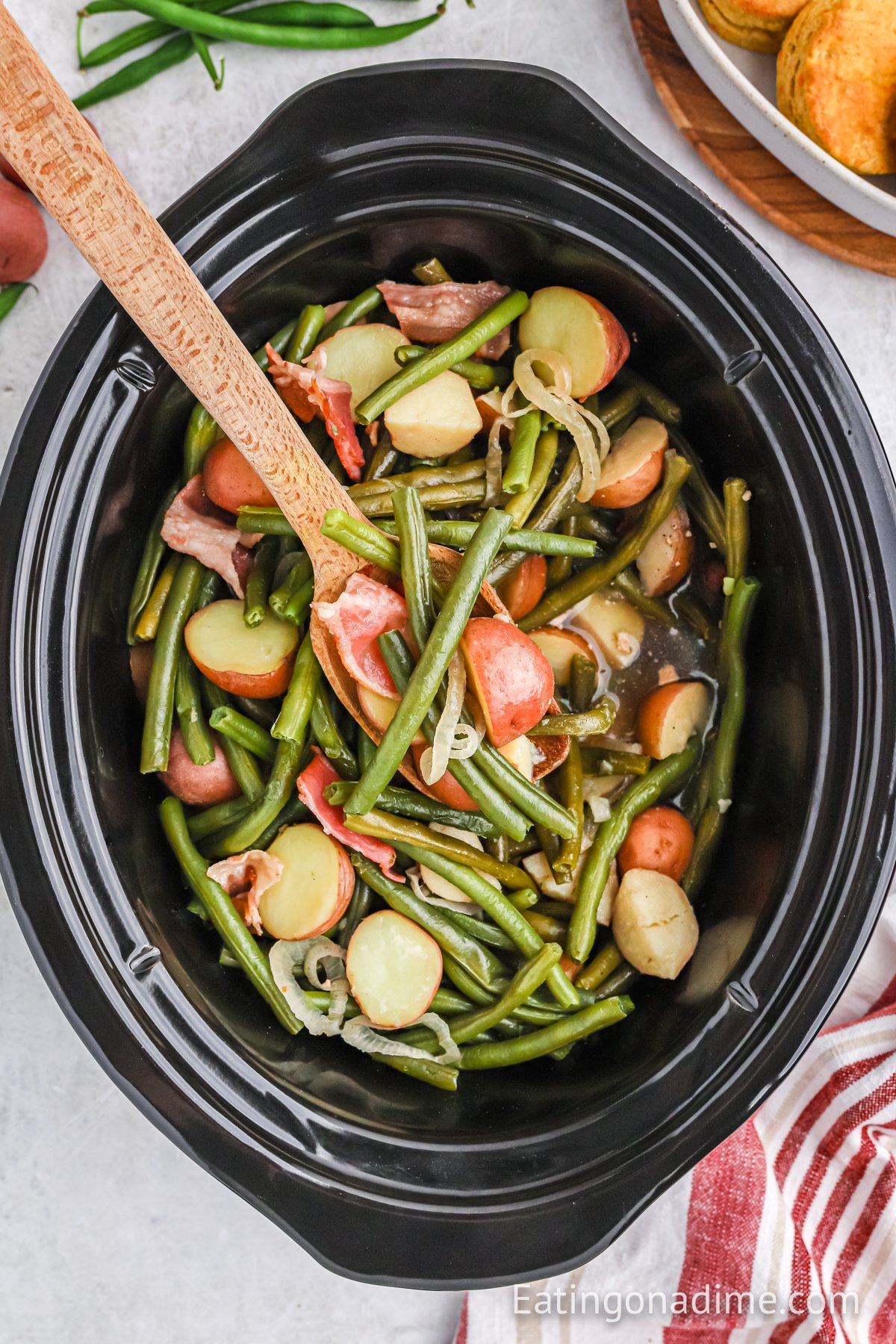 Green and potatoes in a crock pot with a wooden spoon