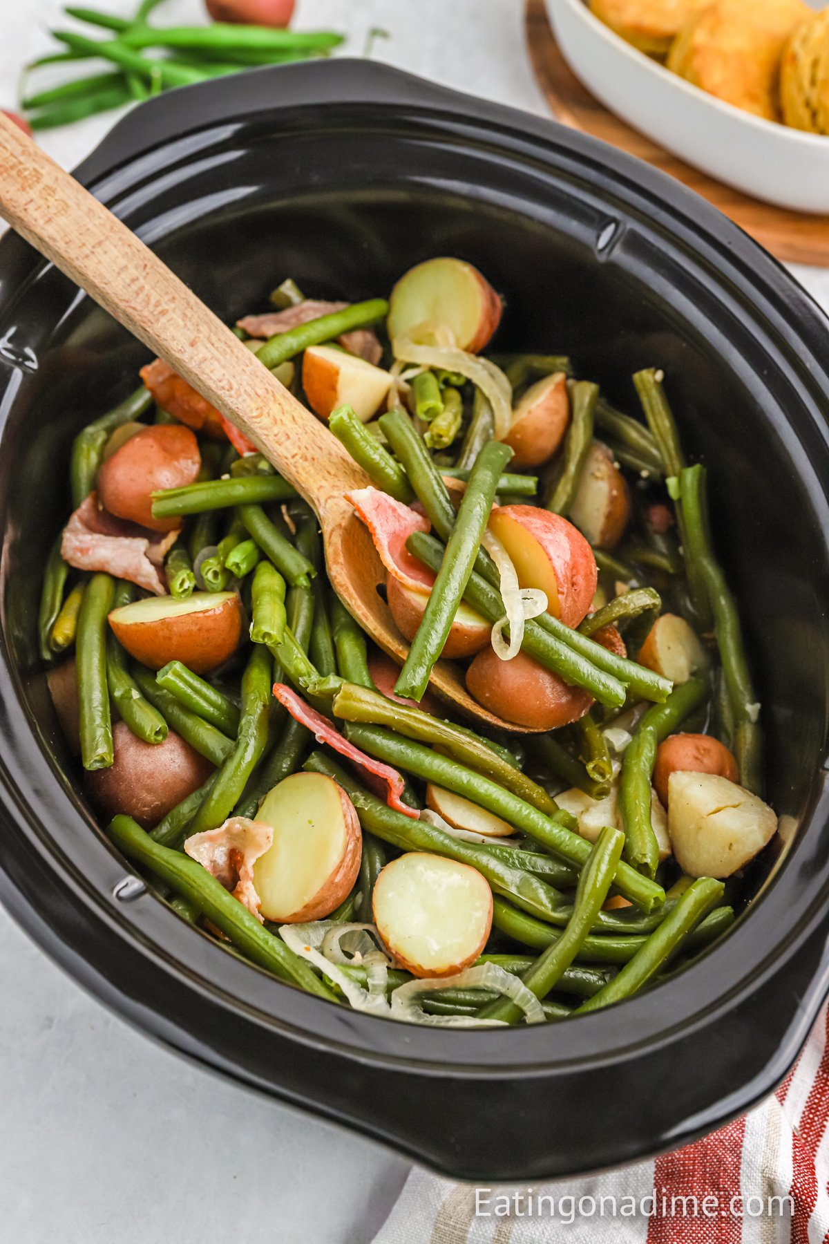 Green and potatoes in a crock pot with a wooden spoon