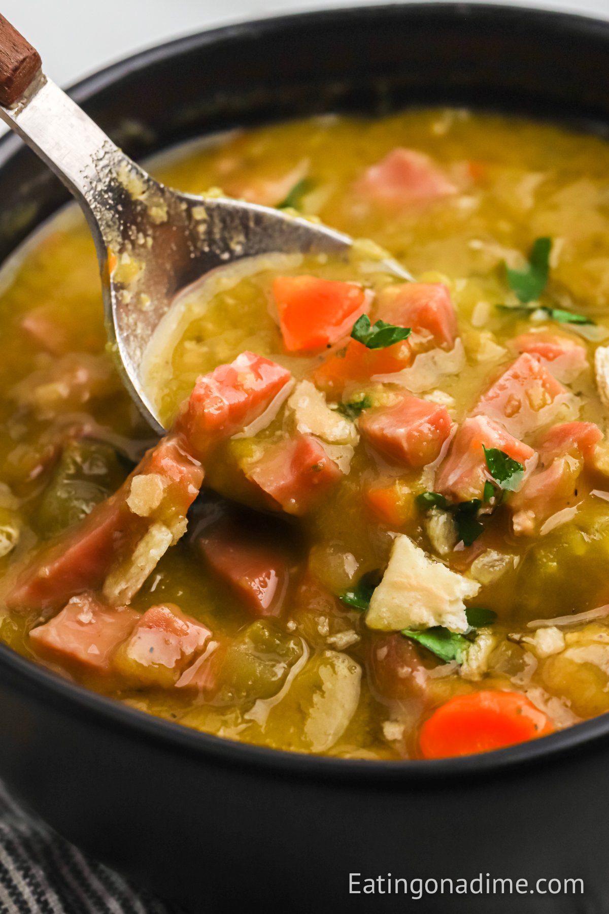 A black bowl of split pea soup with a bite on a spoon