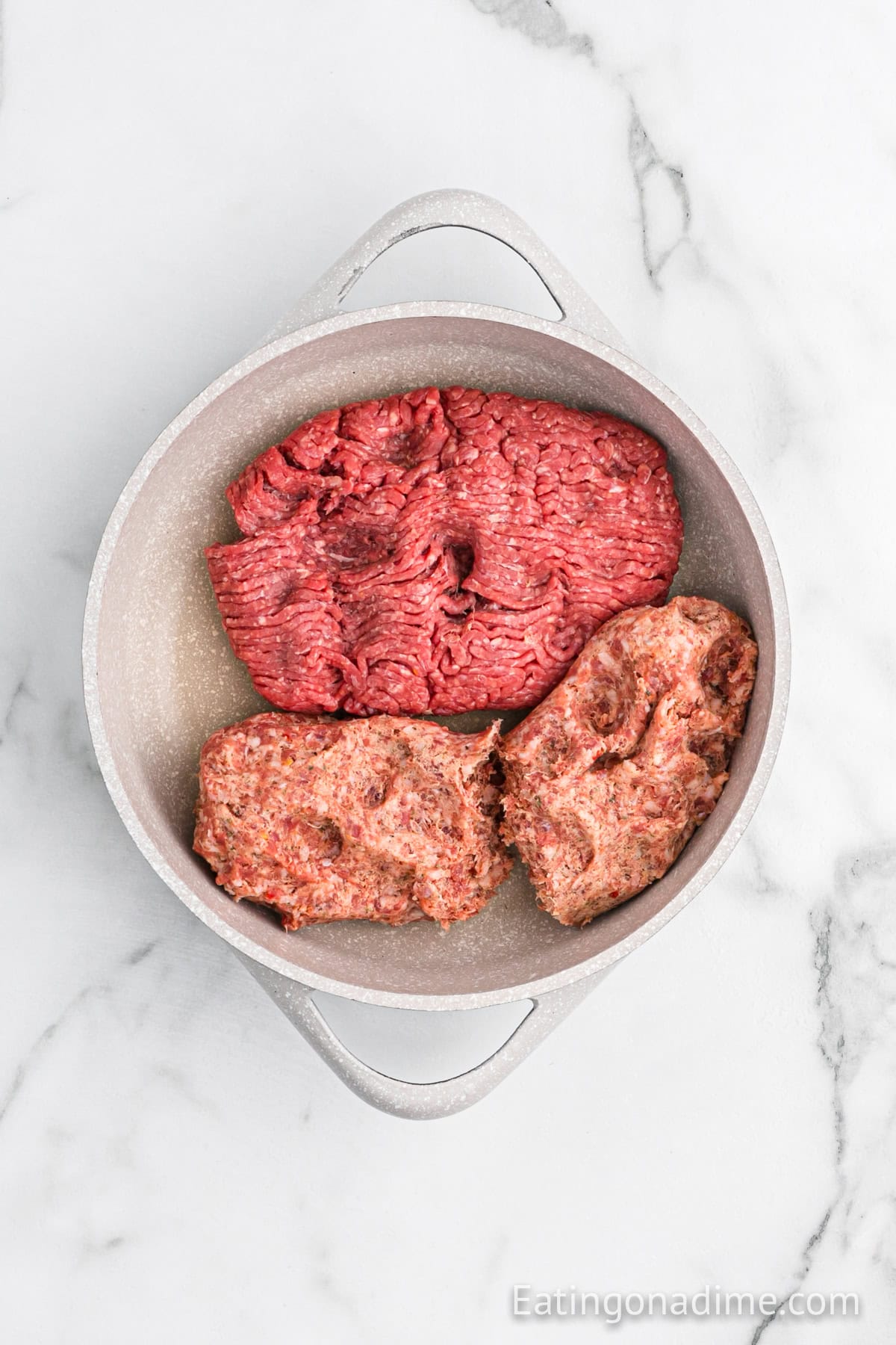 Raw ground beef and raw Italian sausage, perfect for a classic Hanky Panky Recipe, sit separated in a round, light-colored pot on a white marble surfaceโready to be cooked.