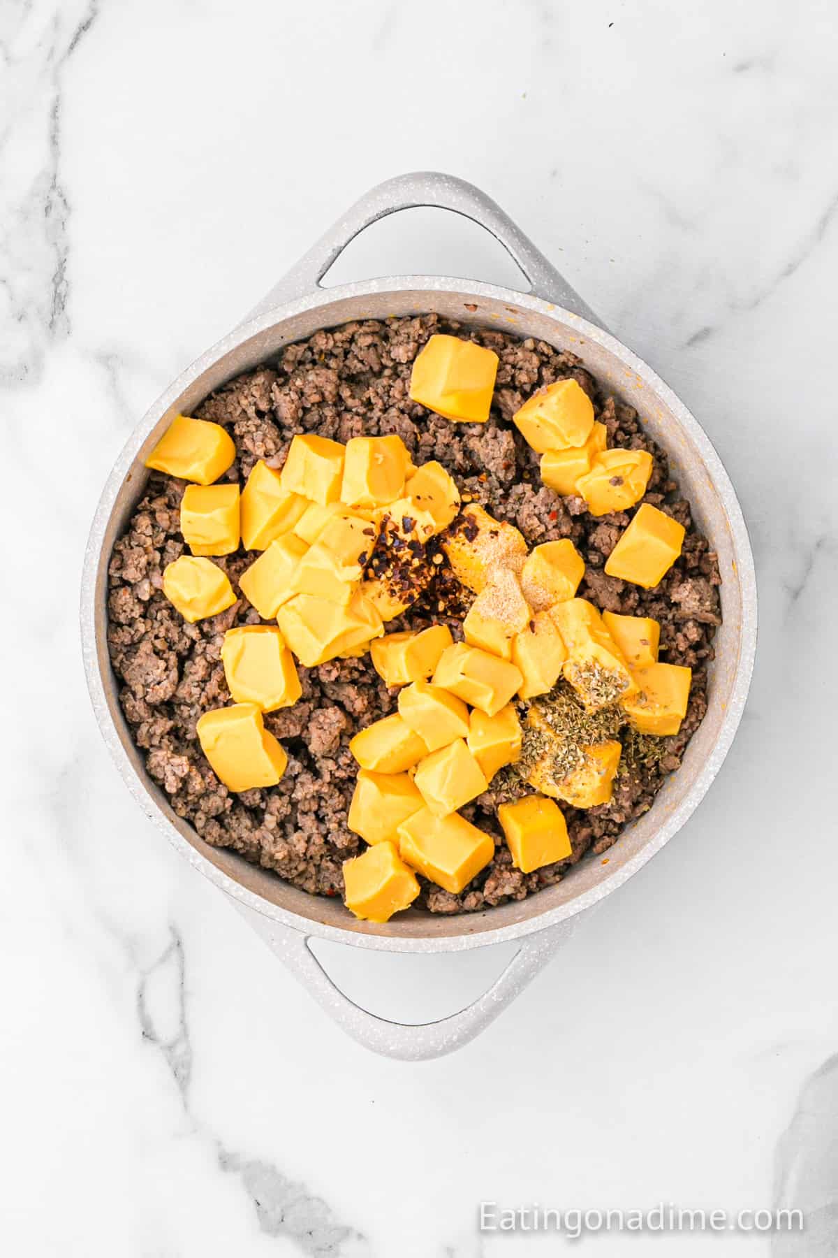 A white pot on a marble surface containing cooked ground beef, cubed yellow cheese, and various seasonings, ready to be mixed together for a classic Hanky Panky Recipe.