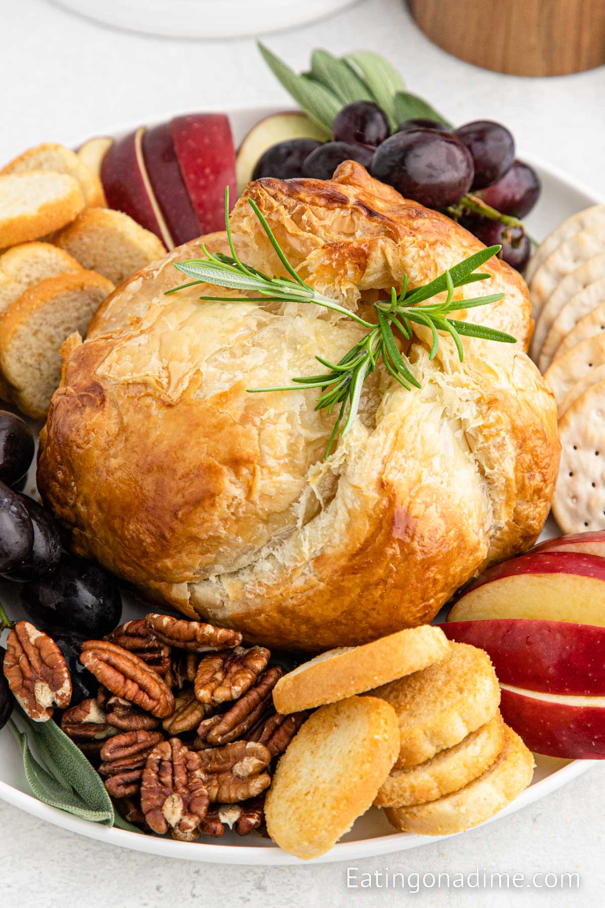 Baked brie in puff pastry on a platter with fresh fruit, crackers and bread