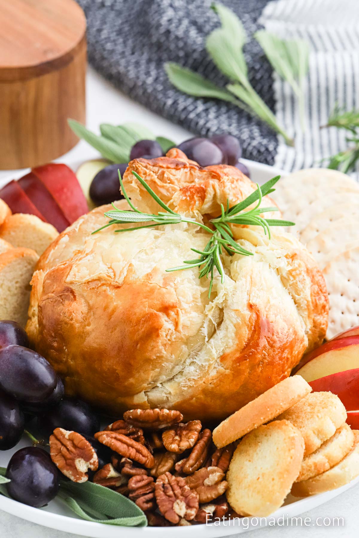 Baked brie in puff pastry on a platter with sides of grapes, crackers and bread