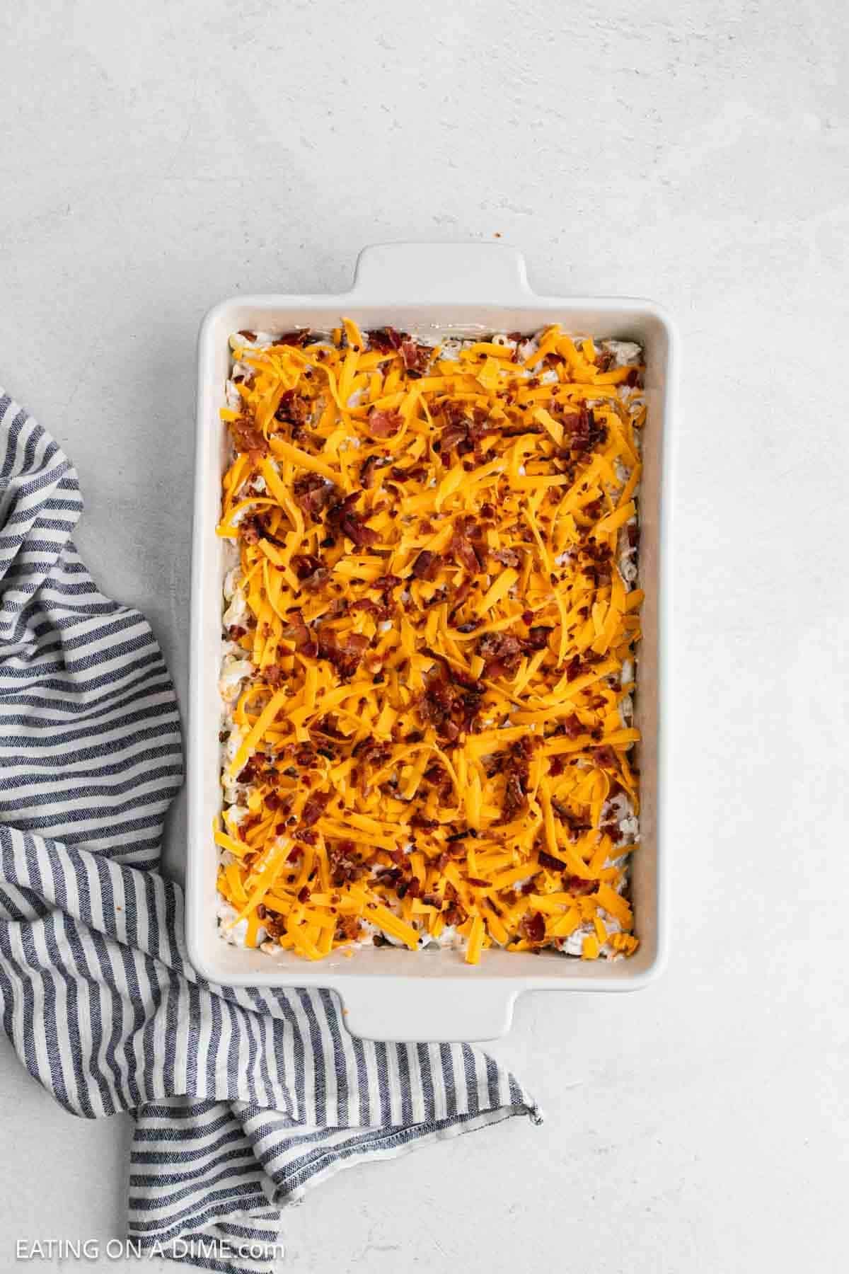 Shredded cheese and chopped bacon topped the pasta mixture in a baking dish.
