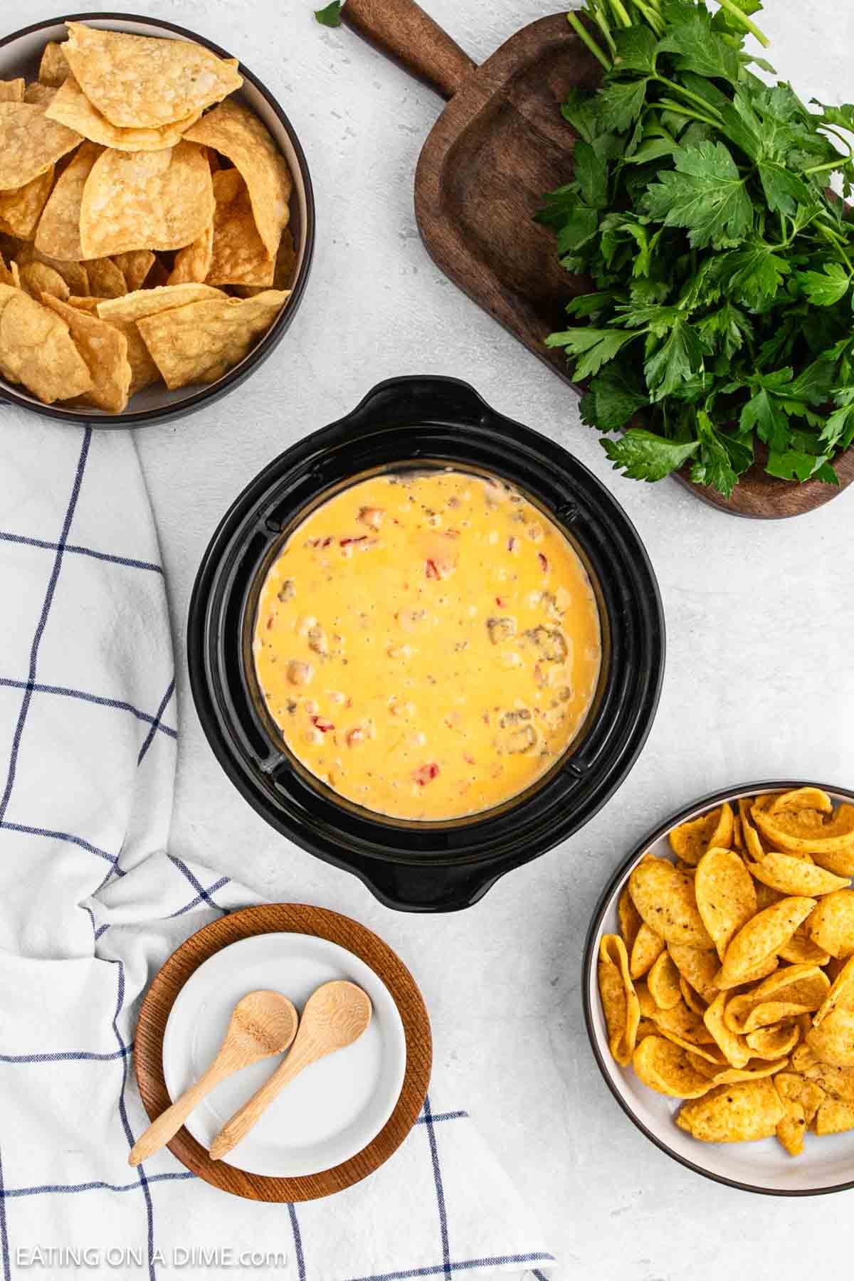 Melted cheese dip in the crockpot with bowls of chips on the side.