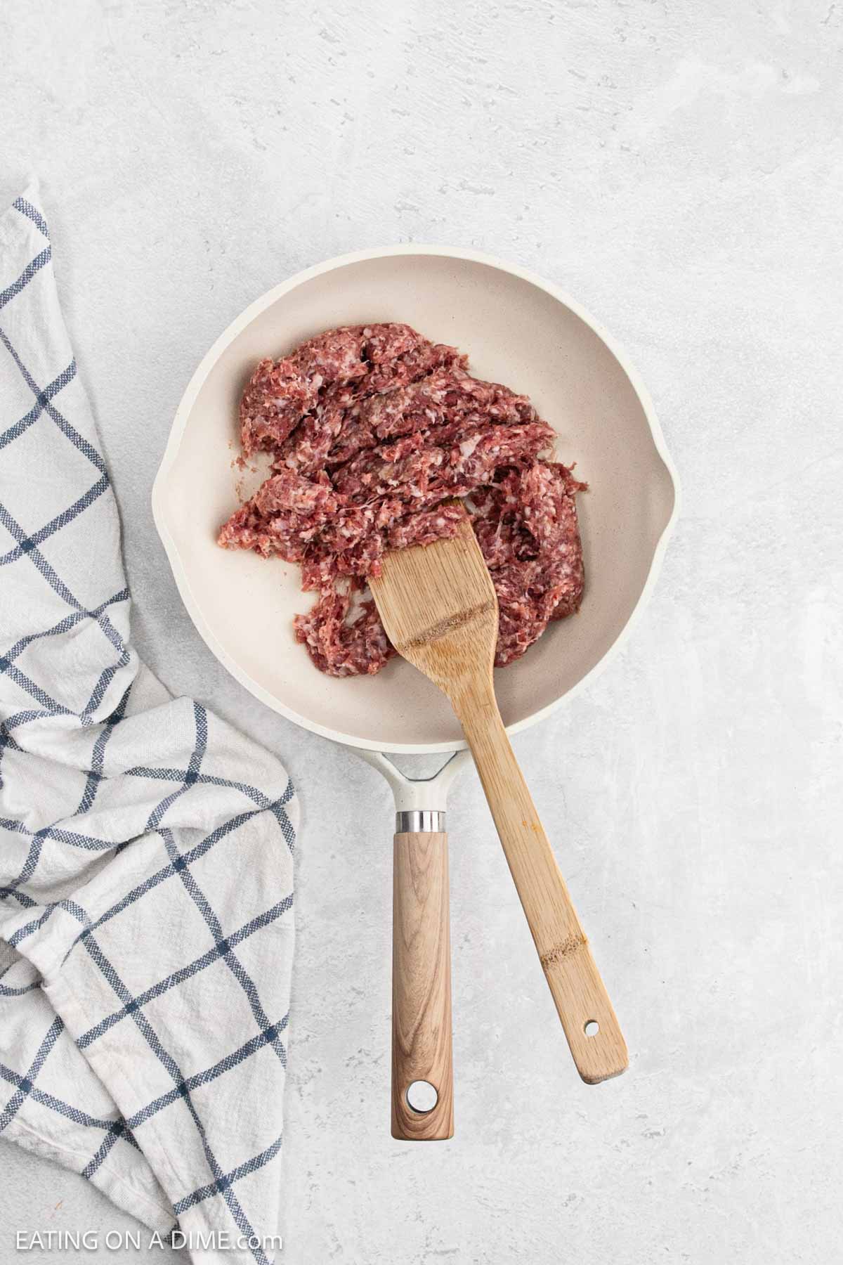 Cooking sausage in a skillet with a wooden spoon.