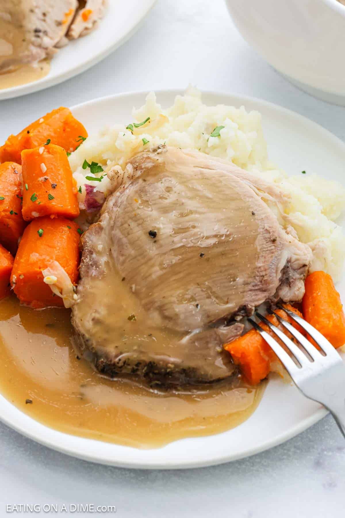 A plate with tender Instant Pot Pork Roast covered in gravy, served alongside mashed potatoes and chunks of cooked carrots. A fork is resting on the plate, spearing a piece of carrot.
