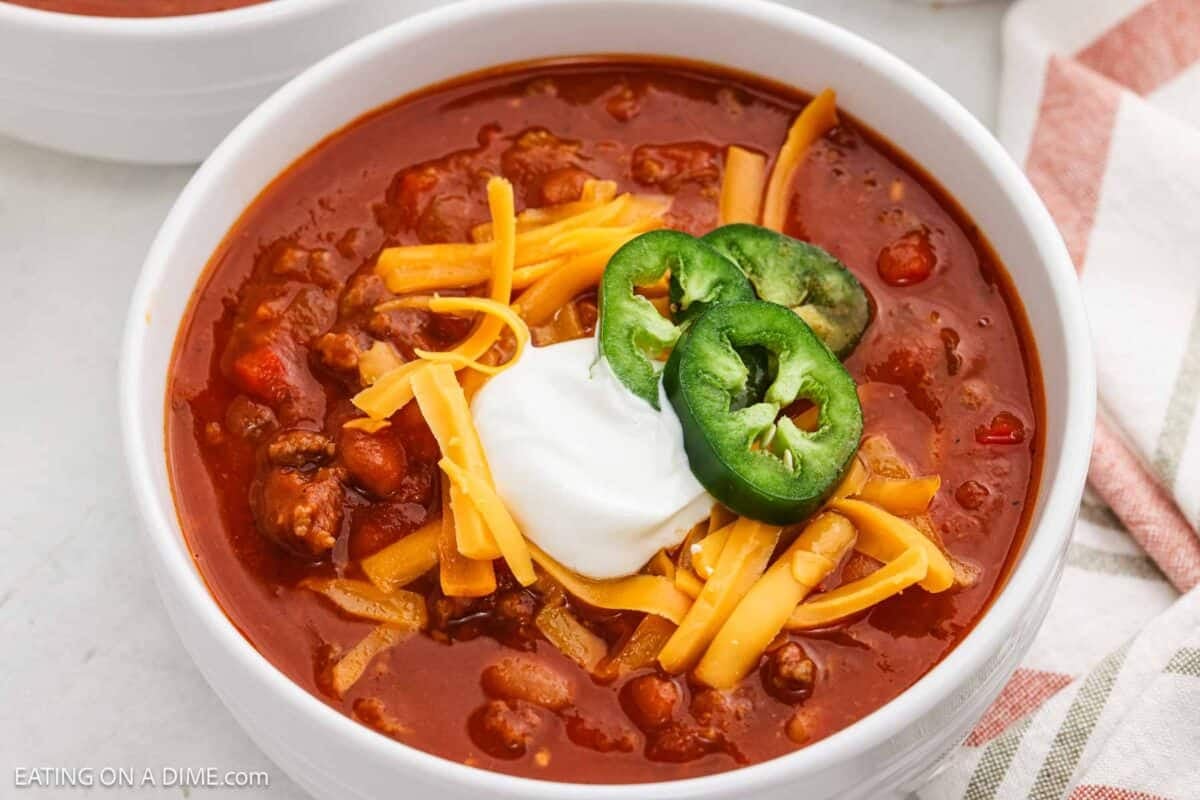 A bowl of pumpkin chili topped with shredded cheese, sour cream, and slice jalapenos.