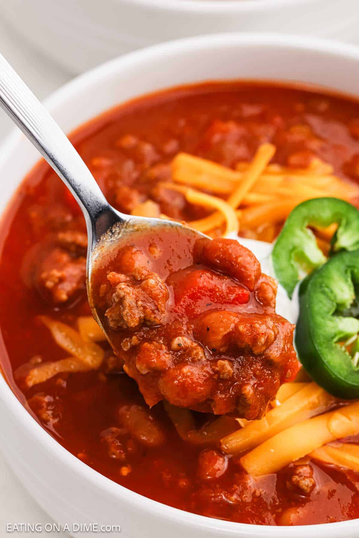 Chili in a bowl topped with shredded cheese, sour cream and slice jalapenos.