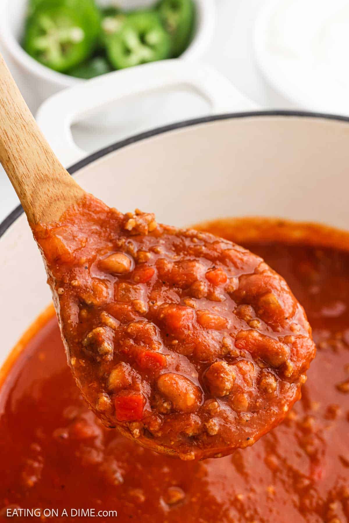 Chili in a large pot with a serving on a wooden spoon.