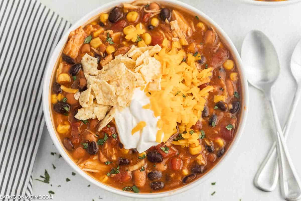 Taco soup in a bowl topped with shredded cheese, crushed tortillas and sour cream.
