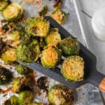A spatula lifts roasted Brussel Sprouts In Oven topped with crispy breadcrumbs from a foil-lined baking sheet, with more sprouts scattered in the background.