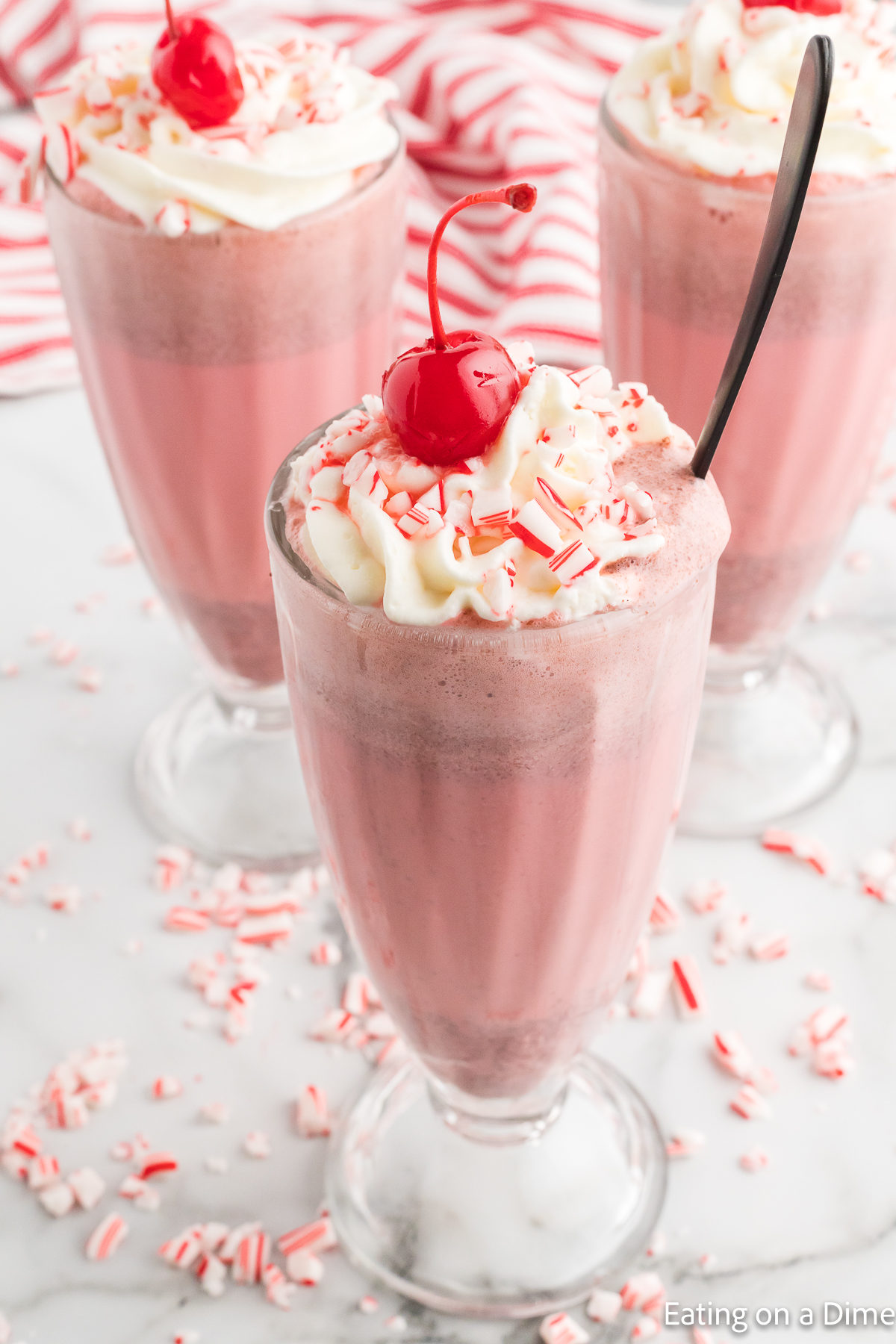 Close up image of Peppermint Milkshake in a glass topped with whipped cream in cherries
