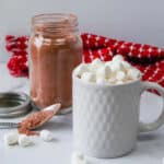 A mug topped with marshmallows with a side of hot chocolate mix in a mason jar