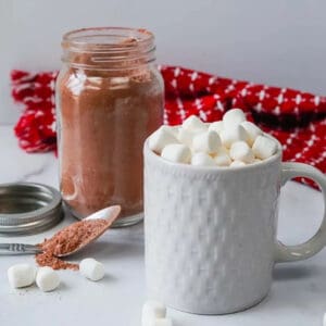 A mug topped with marshmallows with a side of hot chocolate mix in a mason jar