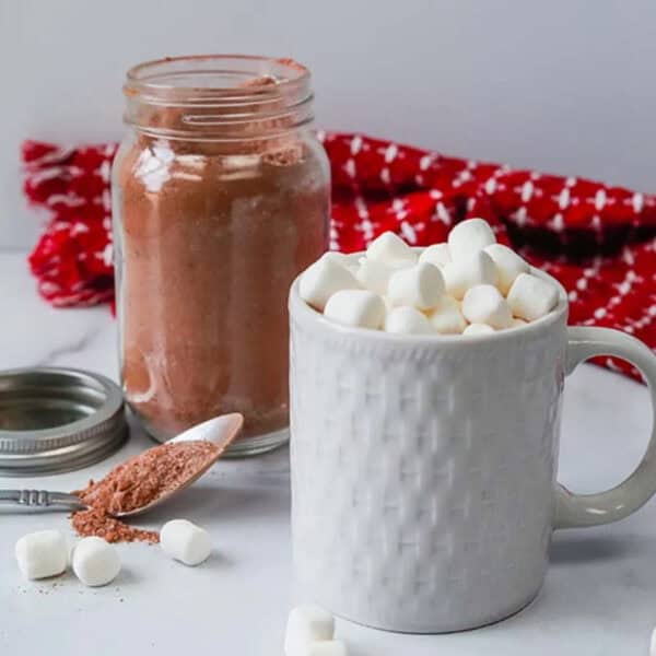 A mug topped with marshmallows with a side of hot chocolate mix in a mason jar