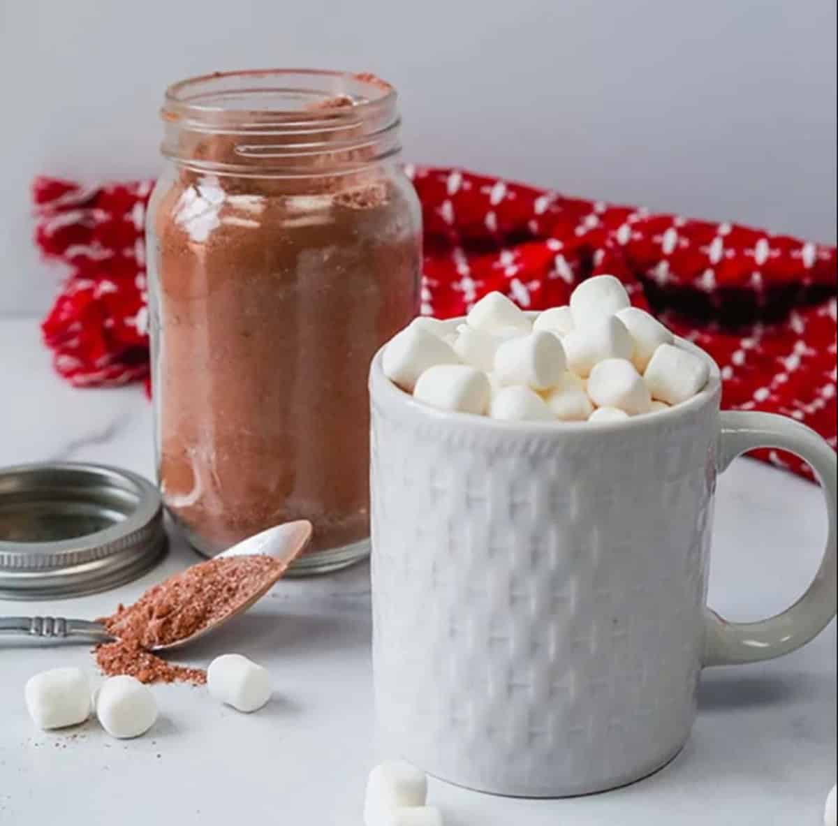 A mug topped with marshmallows with a side of hot chocolate mix in a mason jar