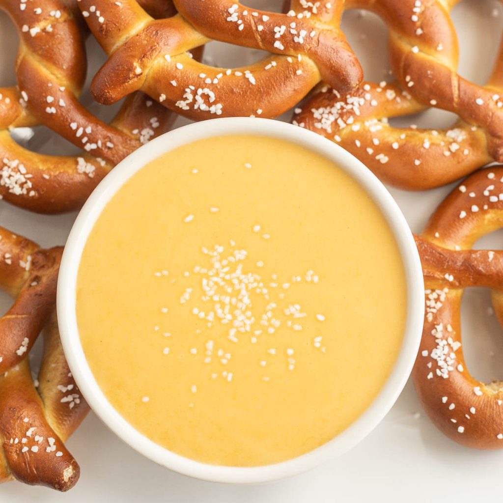 A bowl of cheese dip with a side of pretzels