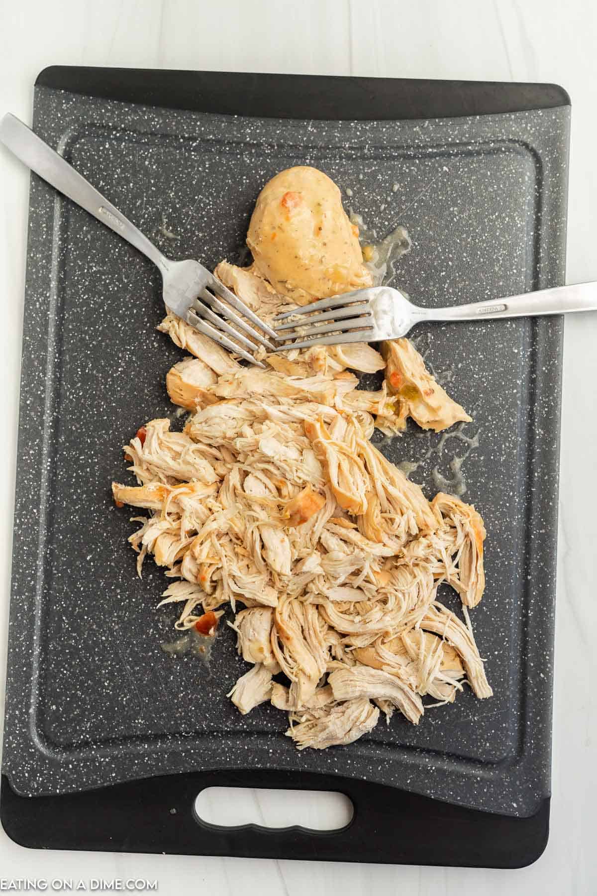 Shredded chicken on a cutting board with two forks