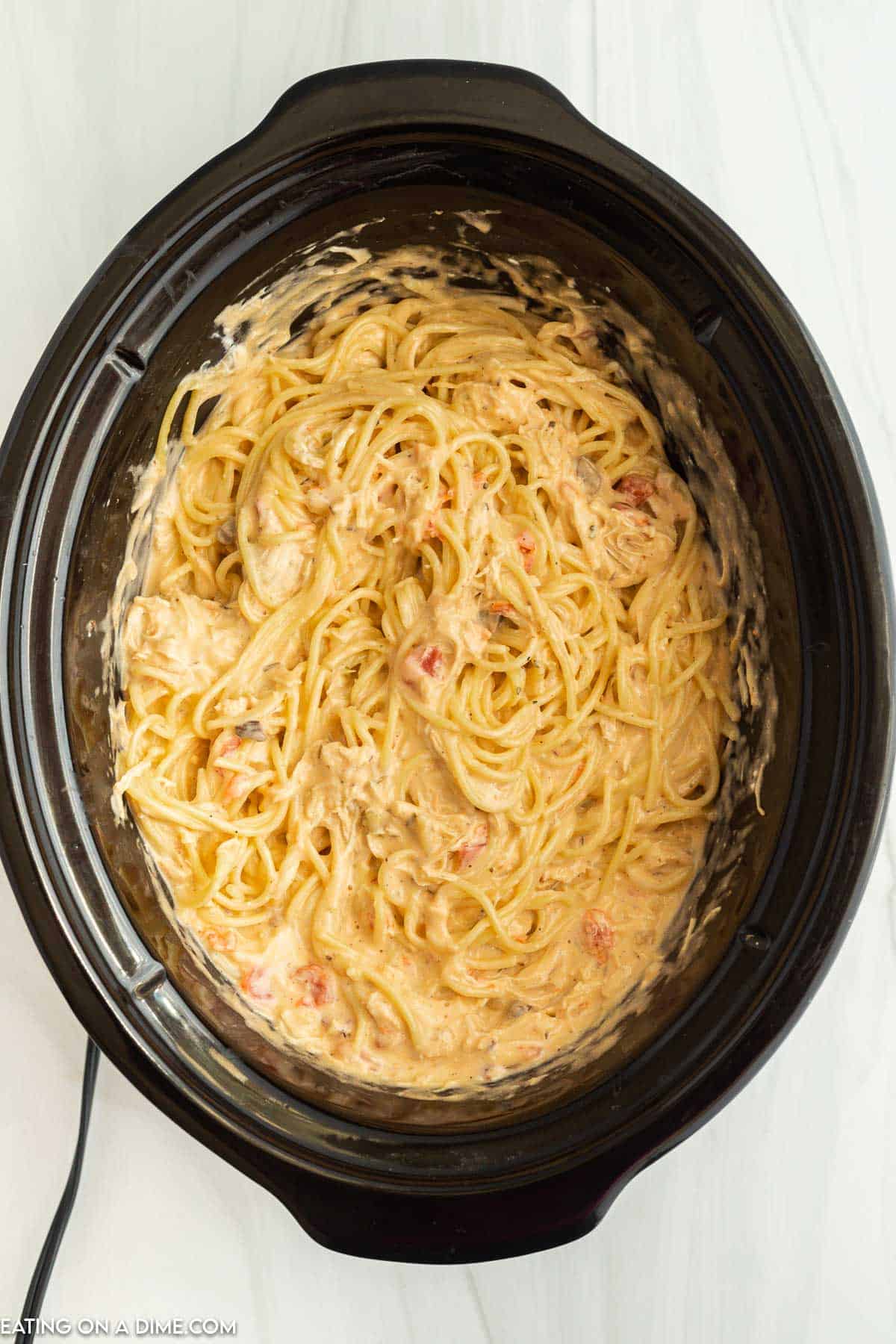 Cooked spaghetti noodles mixed in with the chicken mixture in the slow cooker