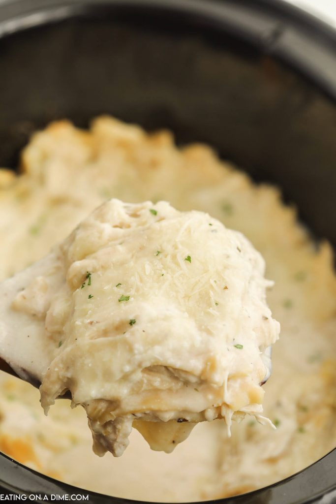 Chicken Alfredo Lasagna in a slow cooker with a serving on a wooden spoon