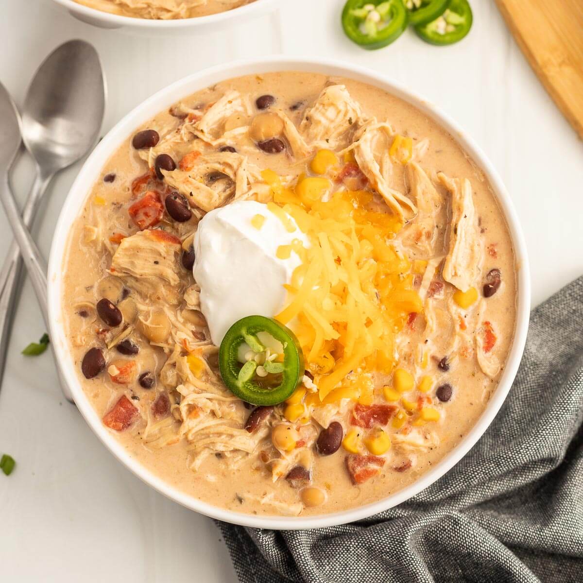 Close up image of a bowl of creamy chicken chili topped with jalapenos, sour cream and cheese