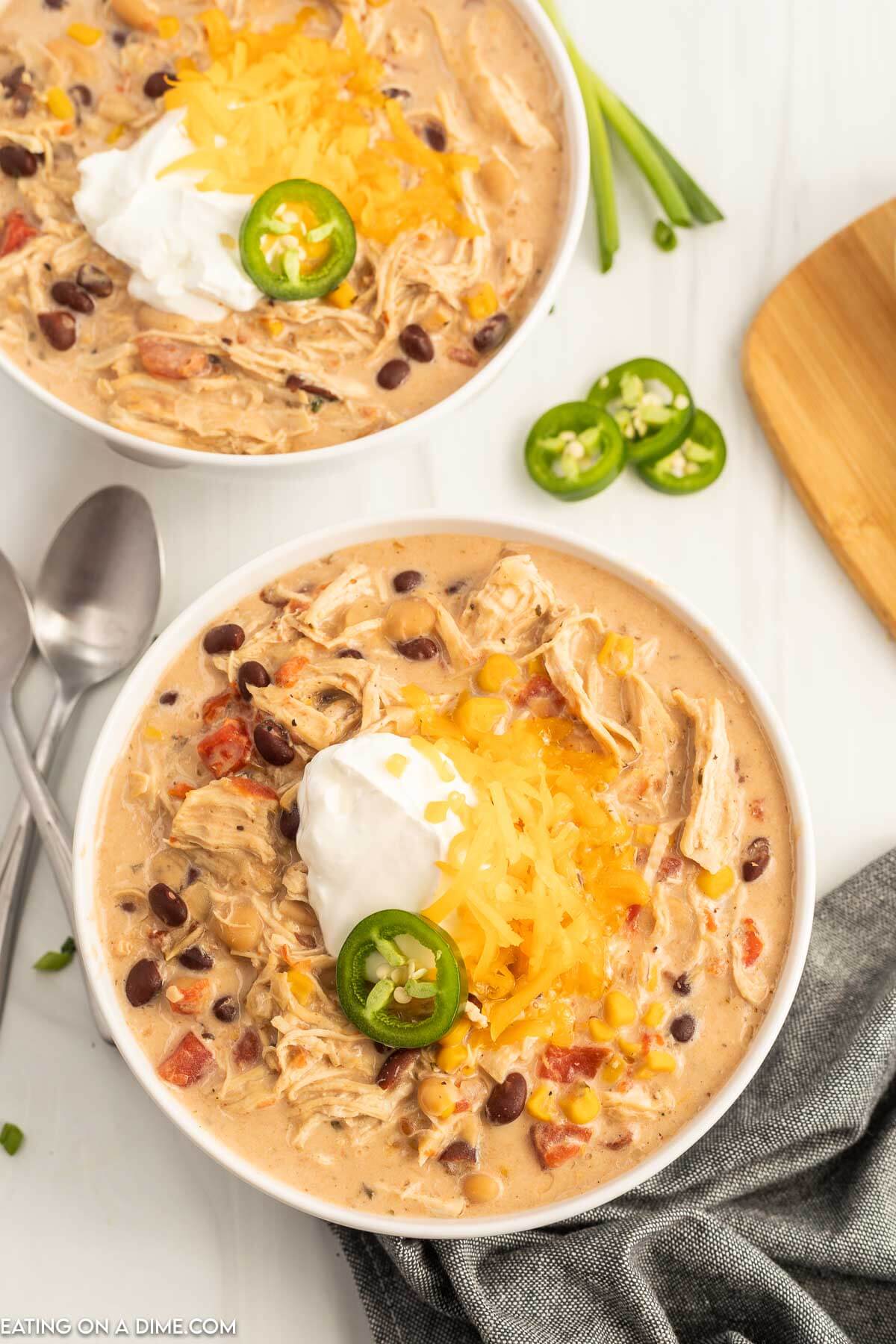 Close up image of a bowl of creamy chicken chili topped with jalapenos, sour cream and cheese