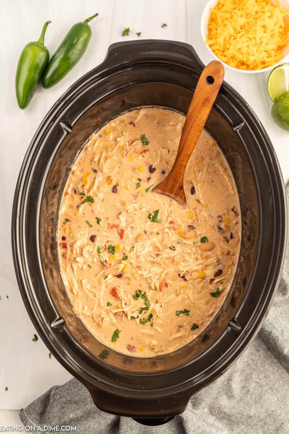 Close up image  of creamy chicken chili topped in slow cooker with a wooden spoon