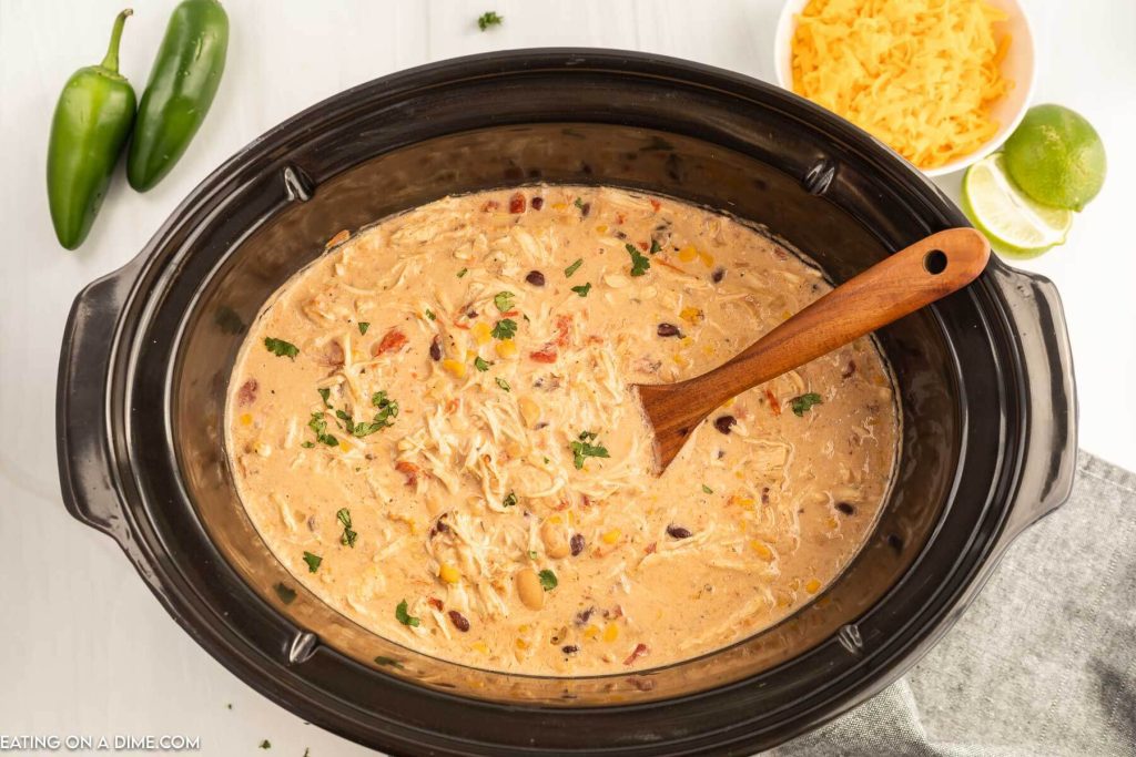 Close up image  of creamy chicken chili in a slow cooker with a wooden spoon