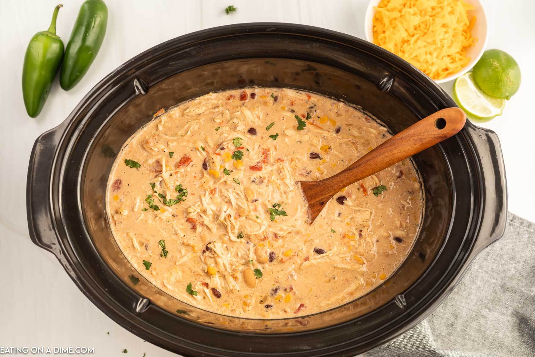 Close up image  of creamy chicken chili in a slow cooker with a wooden spoon