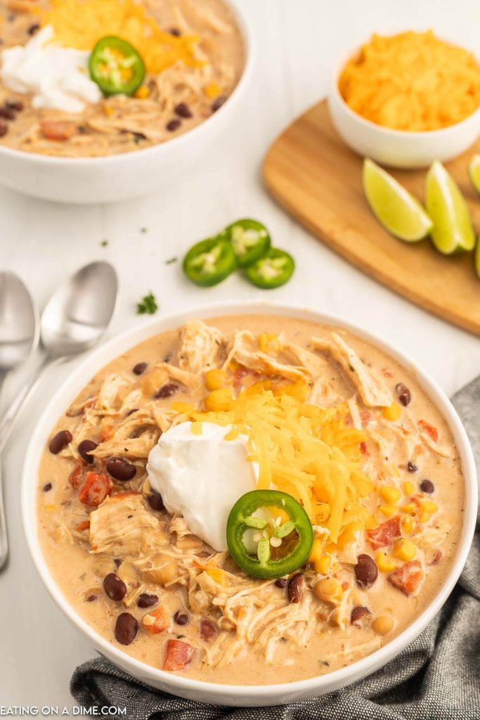 Close up image of a bowl of creamy chicken chili topped with jalapenos, sour cream and cheese
