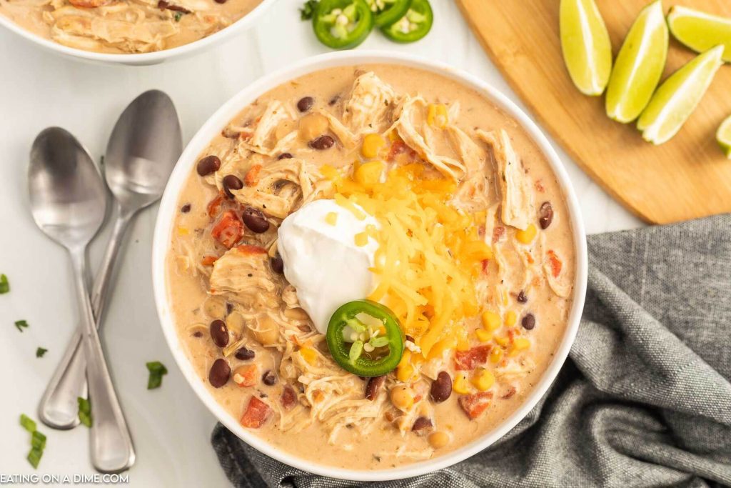 Close up image of a bowl of creamy chicken chili topped with jalapenos, sour cream and cheese