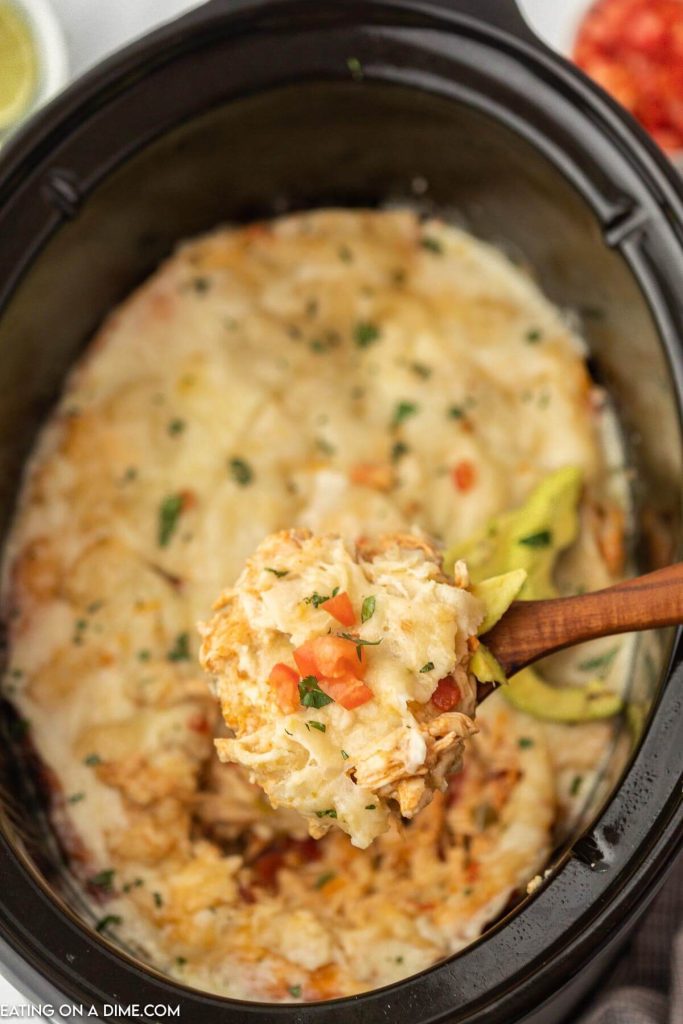 Chicken enchilada casserole in a slow cooker with a serving on a wooden spoon