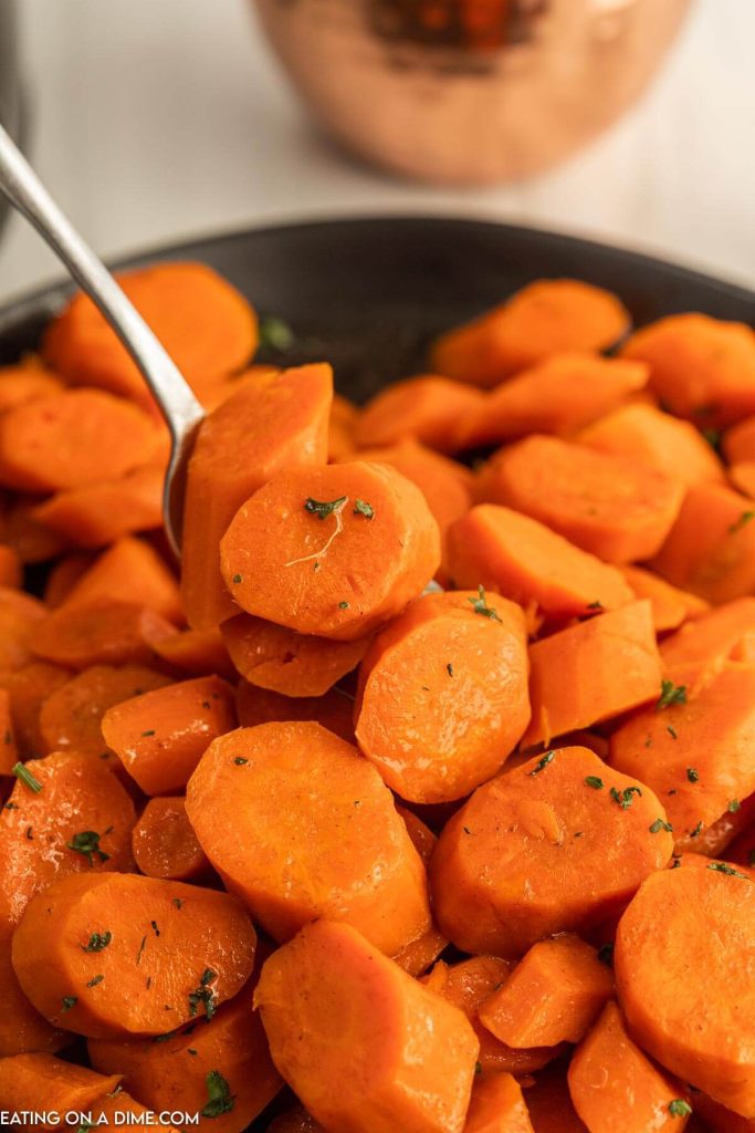 Close up image of glazed carrots in a bowl with a spoon
