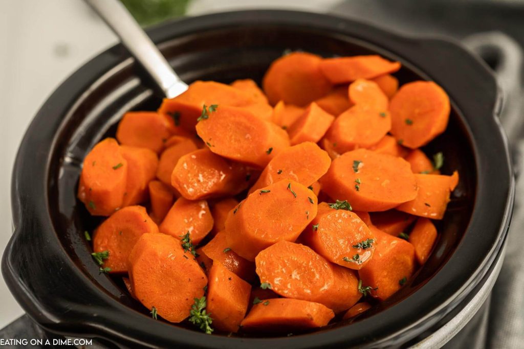 Close up image of glazed carrots in a slow cooker with a spoon
