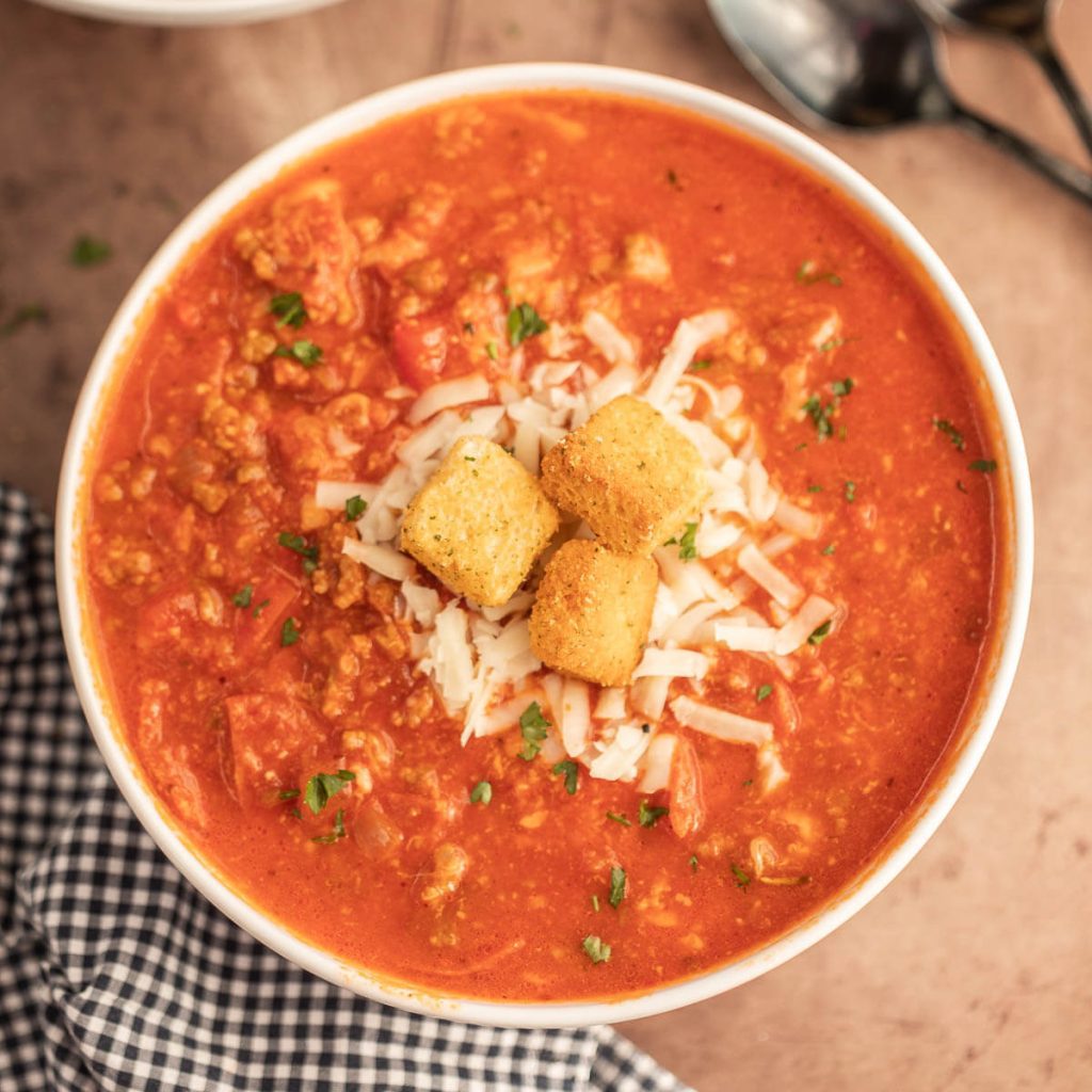 Close up image of Pizza Soup in a white bowl topped with cheese and croutons
