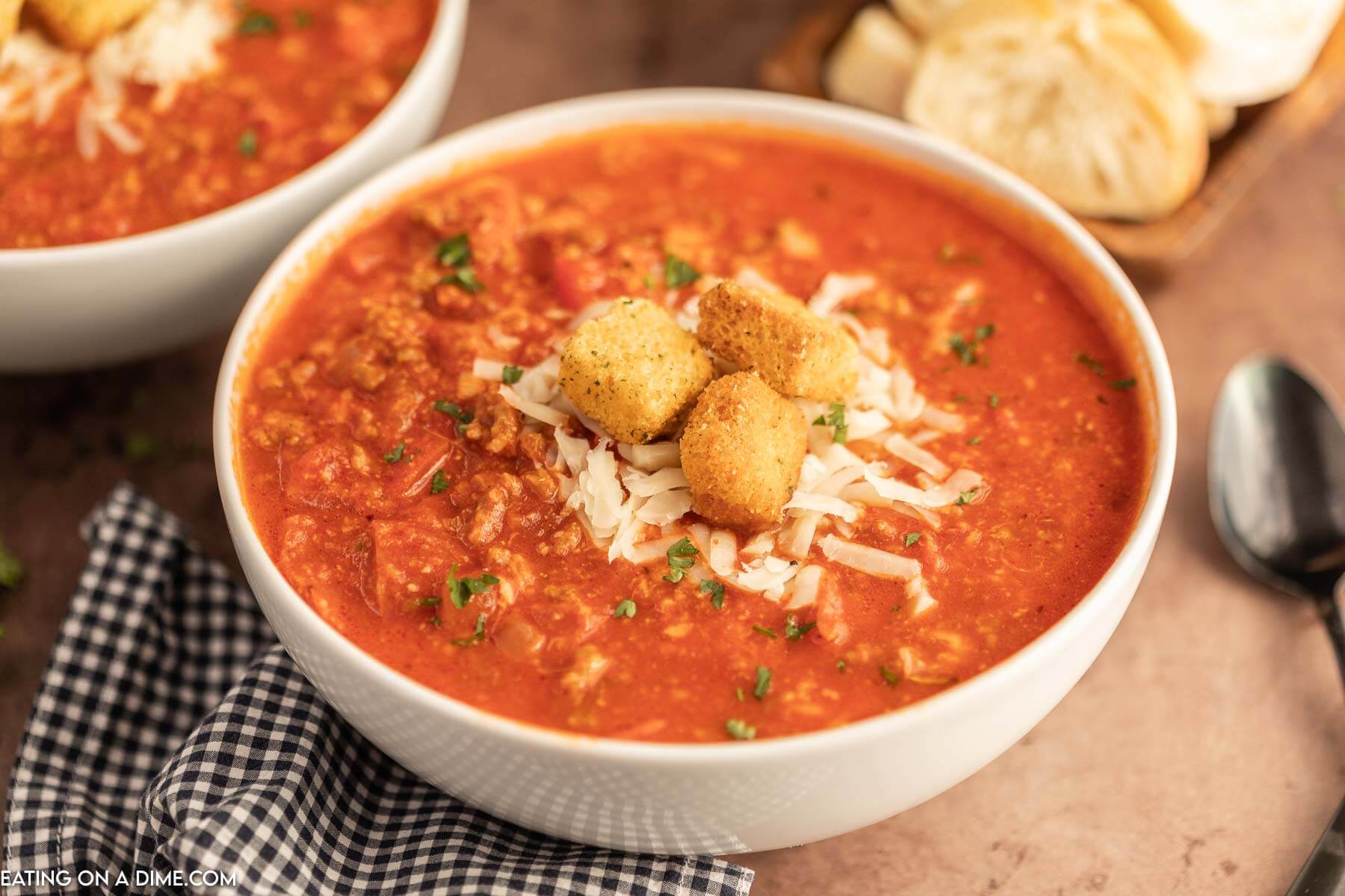 Close up image of Pizza Soup in a white bowl topped with cheese and croutons